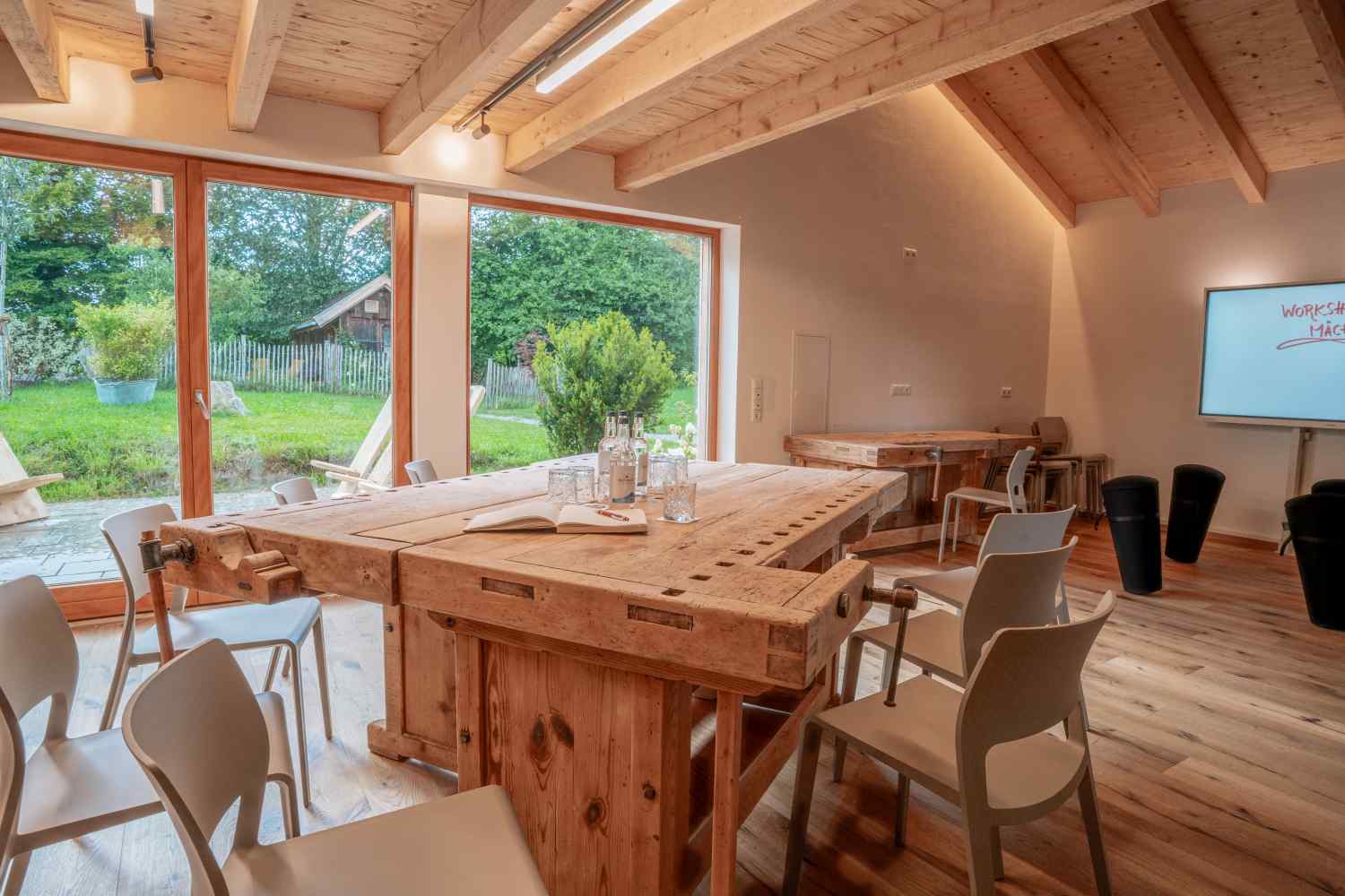 Innenansicht der Denkwerkstatt mit Holztischen, Stühlen und großer Fensterfront mit Blick ins Grüne.