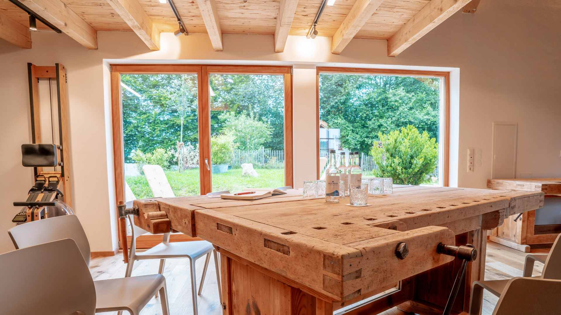 Innenraum der Denkwerkstatt mit Holztisch und Blick durch große Fenster in den Garten.
